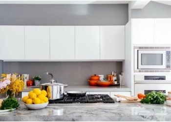 A nice kitchen with pots and pans on the stove and bowls of fruit on the counter